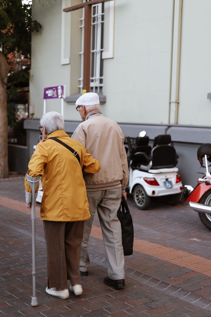Senior couple walking together outdoors, one using a cane, showcasing companionship and support.