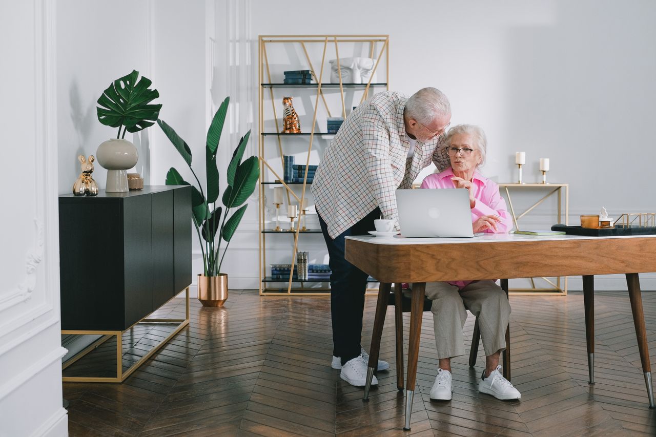 Senior couple using a laptop while discussing something in their modern living room.