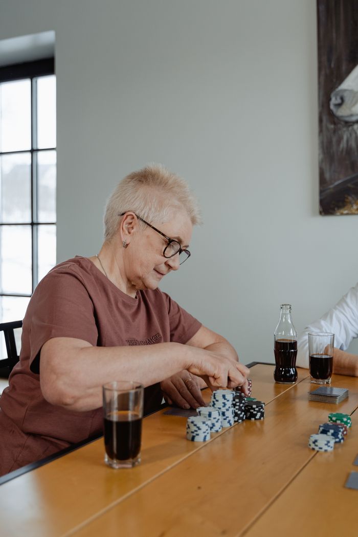 Senior woman enjoying a poker game at home, surrounded by drinks and chips.